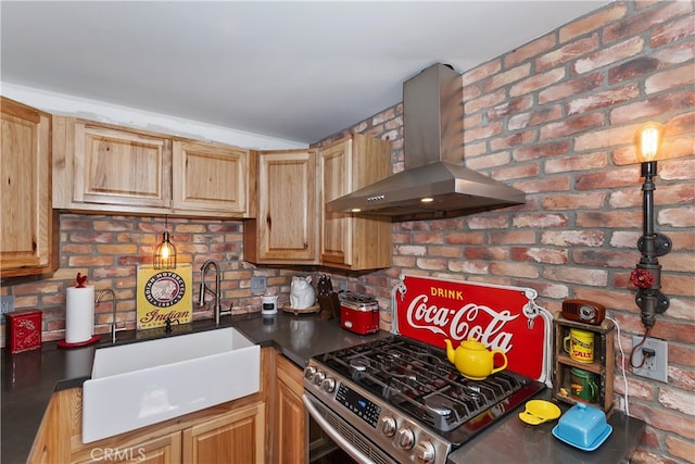 kitchen with dark countertops, a sink, wall chimney range hood, brick wall, and gas range