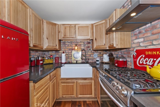 kitchen featuring dark countertops, gas range, fridge, wall chimney range hood, and a sink