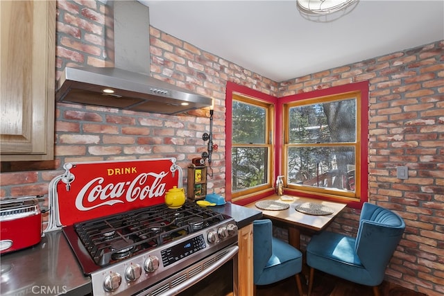 kitchen featuring brick wall, wall chimney exhaust hood, and gas range