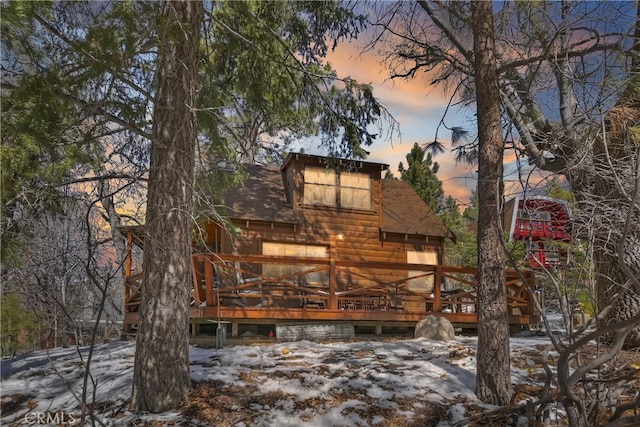 snow covered house featuring roof with shingles and a wooden deck