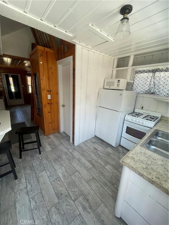 kitchen featuring white appliances, light wood finished floors, wooden walls, light countertops, and a sink