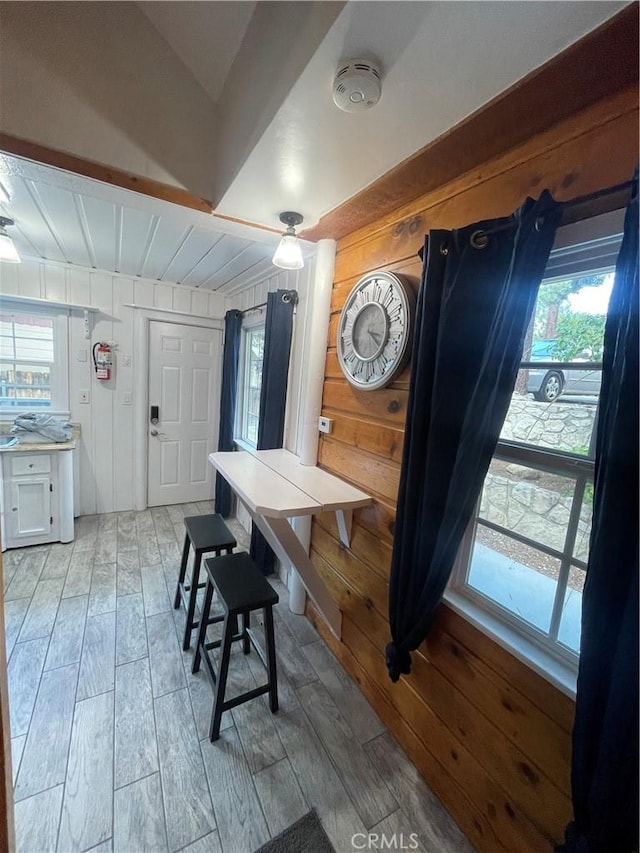 dining area with vaulted ceiling, wooden walls, a wealth of natural light, and wood tiled floor