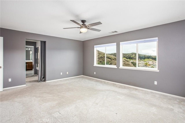 empty room featuring baseboards, light colored carpet, visible vents, and a ceiling fan