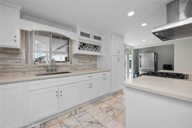 kitchen featuring a sink, white cabinetry, freestanding refrigerator, wall chimney range hood, and glass insert cabinets