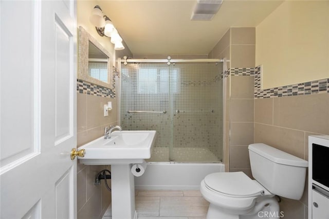 full bath with tile walls, toilet, tile patterned floors, and bath / shower combo with glass door