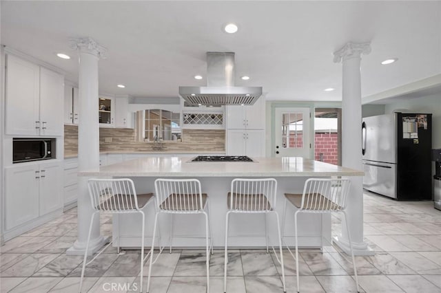 kitchen featuring ornate columns, gas stovetop, freestanding refrigerator, marble finish floor, and island range hood