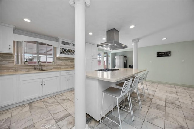 kitchen with a kitchen bar, island range hood, stainless steel appliances, ornate columns, and a sink