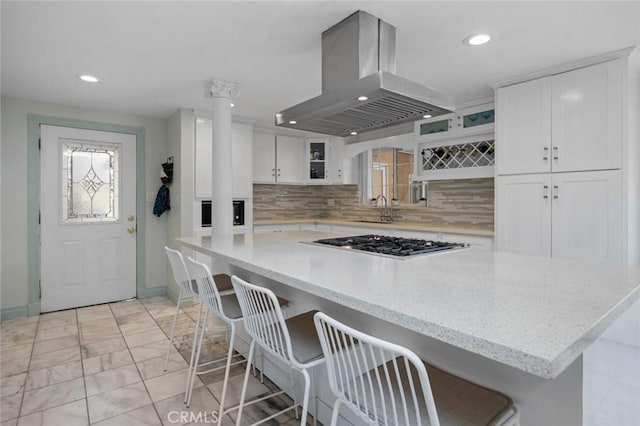 kitchen featuring a sink, white cabinetry, a breakfast bar area, island range hood, and stainless steel gas cooktop