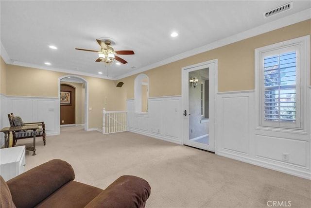 living room featuring arched walkways, light carpet, crown molding, and a ceiling fan