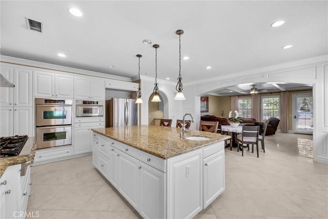 kitchen featuring an island with sink, arched walkways, white cabinets, stainless steel appliances, and a sink