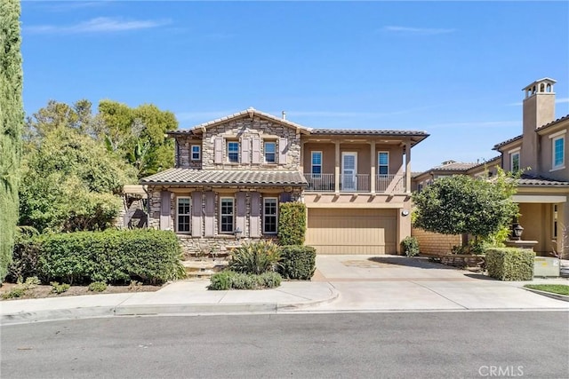 mediterranean / spanish home featuring stucco siding, a tile roof, stone siding, concrete driveway, and an attached garage