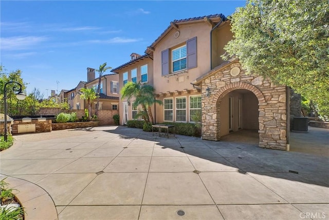 mediterranean / spanish-style house featuring a tiled roof, stucco siding, stone siding, an outdoor kitchen, and a patio