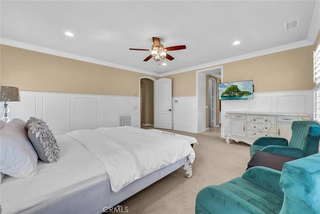 bedroom featuring visible vents, crown molding, light colored carpet, wainscoting, and arched walkways