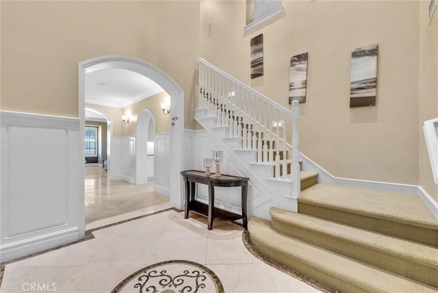 stairs featuring a wainscoted wall, a high ceiling, arched walkways, crown molding, and a decorative wall