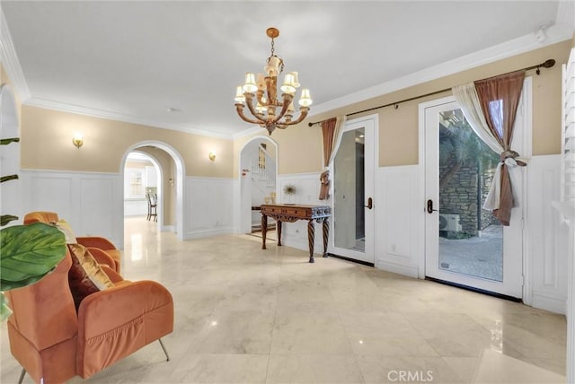 interior space featuring a wainscoted wall, ornamental molding, arched walkways, an inviting chandelier, and a decorative wall