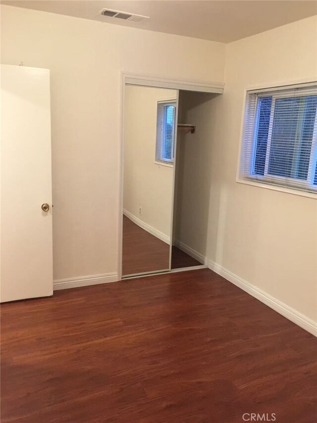 unfurnished bedroom featuring a closet, visible vents, baseboards, and wood finished floors