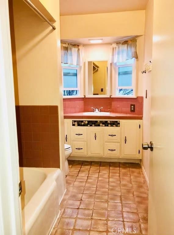 full bath featuring toilet, a tub, decorative backsplash, and vanity