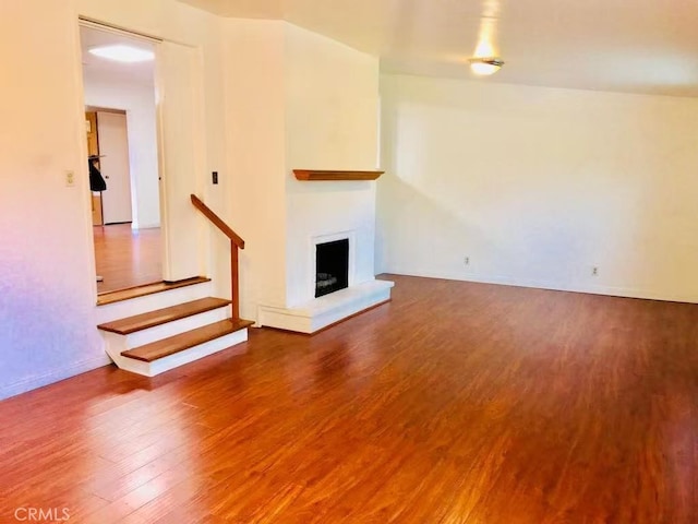 unfurnished living room with stairway, baseboards, a fireplace with raised hearth, and wood finished floors