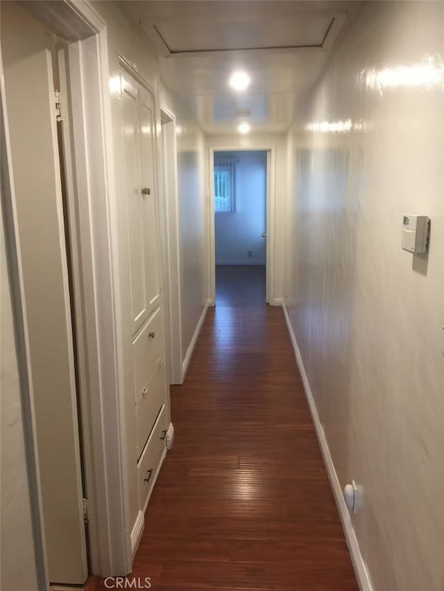 hall featuring attic access, baseboards, and dark wood finished floors