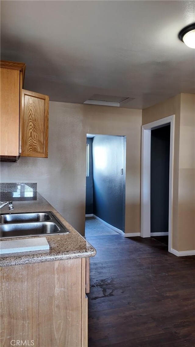 kitchen featuring brown cabinetry, dark wood-type flooring, baseboards, and a sink