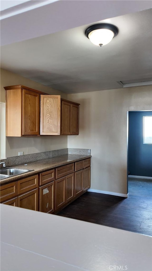 kitchen with brown cabinetry, dark wood-style flooring, baseboards, and a sink