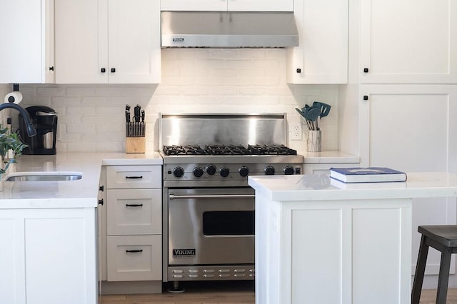 kitchen with premium stove, a sink, under cabinet range hood, and white cabinetry