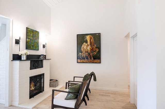 living area with a brick fireplace, a high ceiling, baseboards, and wood finished floors