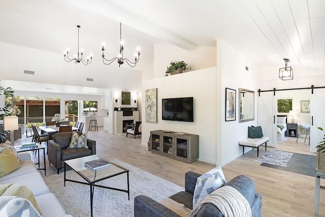 living area featuring a barn door, visible vents, an inviting chandelier, light wood-style floors, and beam ceiling