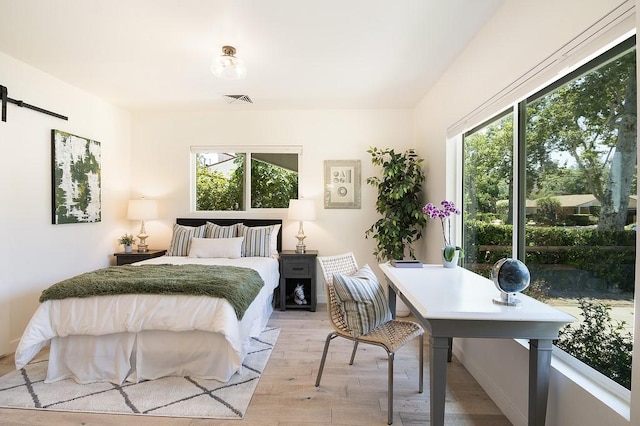 bedroom with light wood finished floors, a barn door, and visible vents