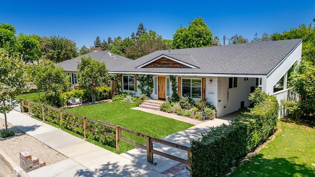 ranch-style house featuring roof with shingles, a front yard, and fence