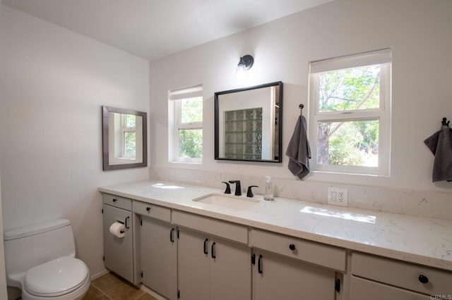 bathroom with toilet, tile patterned flooring, a wealth of natural light, and vanity