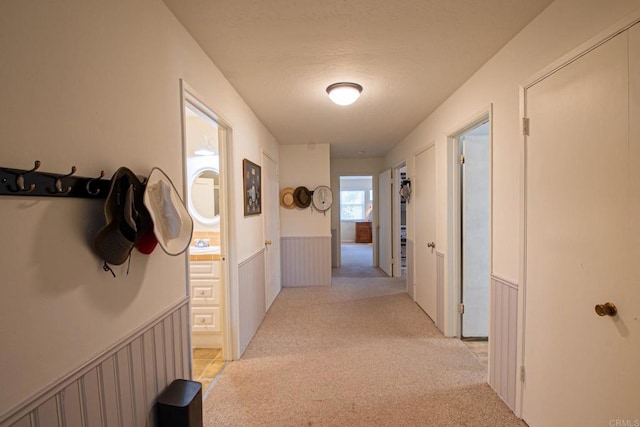 hallway featuring wainscoting and light carpet