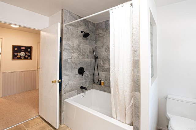 full bathroom featuring a wainscoted wall, shower / bathtub combination with curtain, toilet, and tile patterned floors