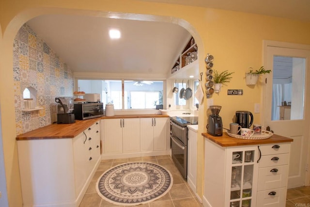 kitchen featuring arched walkways, light tile patterned floors, butcher block counters, appliances with stainless steel finishes, and vaulted ceiling