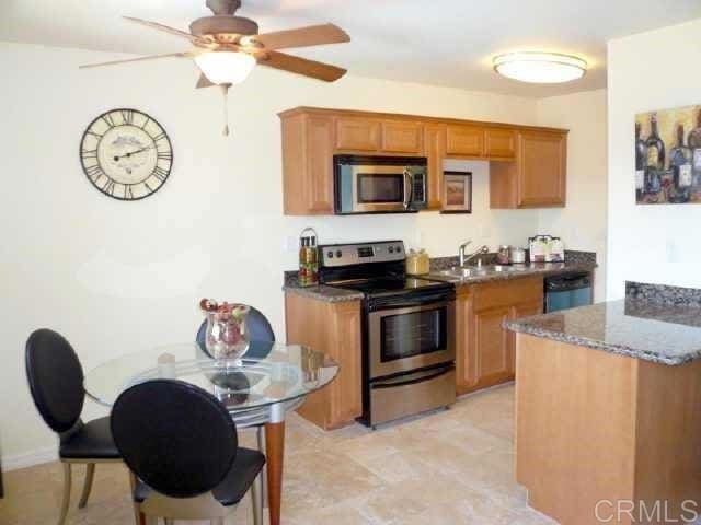 kitchen featuring stainless steel appliances, brown cabinetry, a ceiling fan, a sink, and dark stone counters