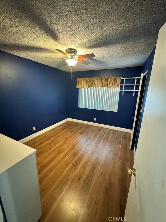 unfurnished bedroom featuring ceiling fan, a textured ceiling, baseboards, and wood finished floors