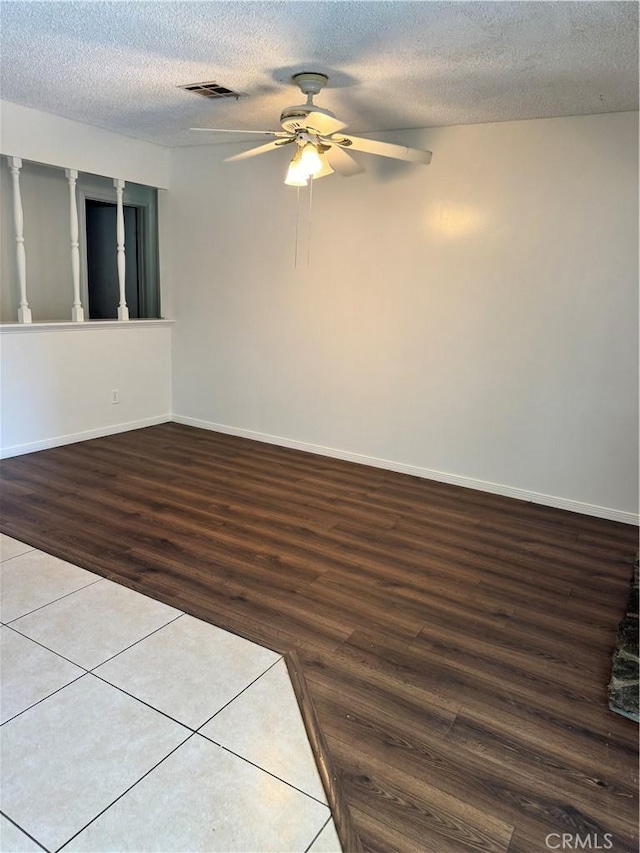 spare room with a textured ceiling, wood finished floors, visible vents, and baseboards