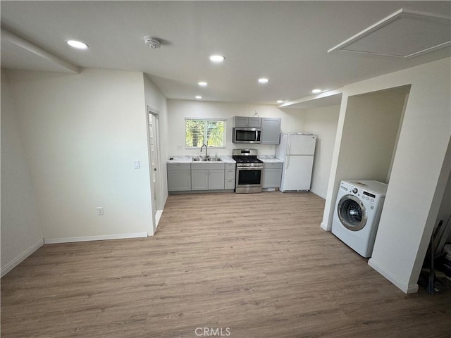 kitchen featuring light wood-style flooring, gray cabinetry, stainless steel appliances, a sink, and washer / dryer