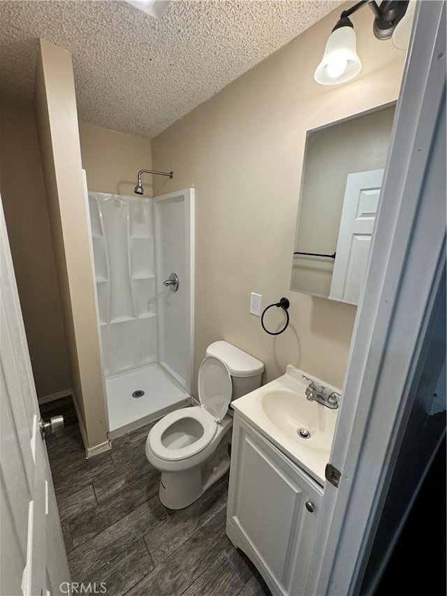 bathroom with wood finish floors, toilet, a stall shower, a textured ceiling, and vanity