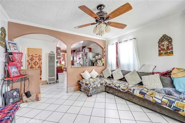 living area with a ceiling fan, tile patterned flooring, ornamental molding, and a textured ceiling