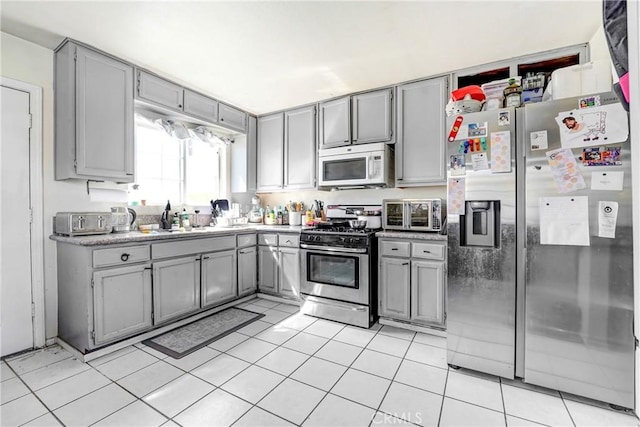 kitchen featuring light countertops, light tile patterned floors, gray cabinetry, a sink, and appliances with stainless steel finishes
