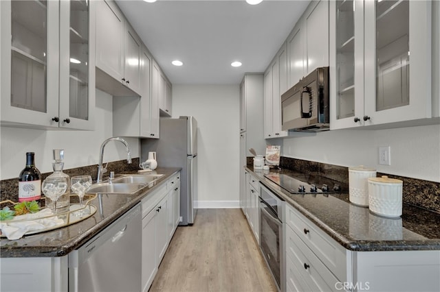 kitchen with dark stone counters, black appliances, a sink, and light wood-style flooring