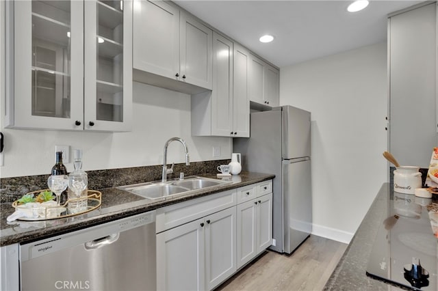 kitchen with recessed lighting, a sink, light wood-style floors, appliances with stainless steel finishes, and glass insert cabinets