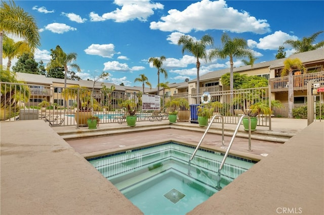 community pool featuring a residential view, fence, and a hot tub