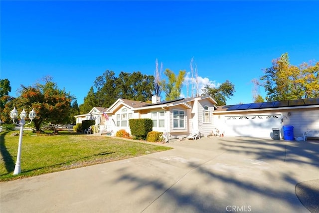 ranch-style house featuring concrete driveway, a front lawn, an attached garage, and roof mounted solar panels