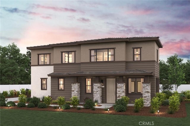 view of front facade featuring a yard, stone siding, fence, and stucco siding