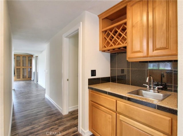 kitchen featuring arched walkways, decorative backsplash, dark wood-type flooring, a sink, and baseboards