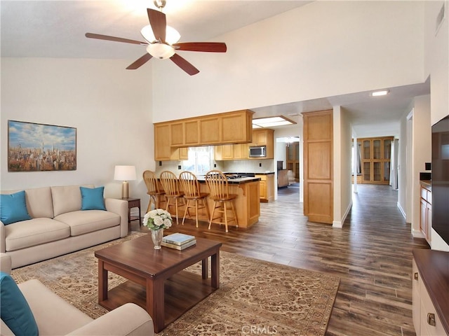 living room featuring dark wood finished floors, a towering ceiling, baseboards, and ceiling fan