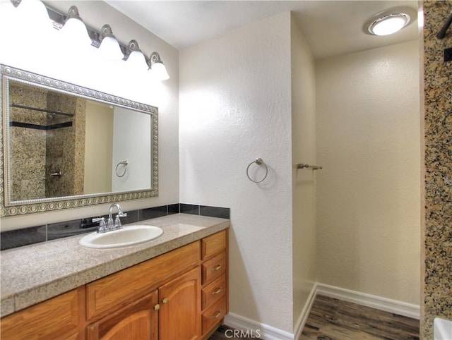 full bath with a textured wall, wood finished floors, vanity, baseboards, and walk in shower