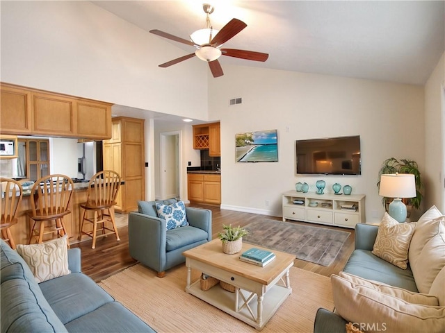 living area with baseboards, visible vents, a ceiling fan, wood finished floors, and high vaulted ceiling